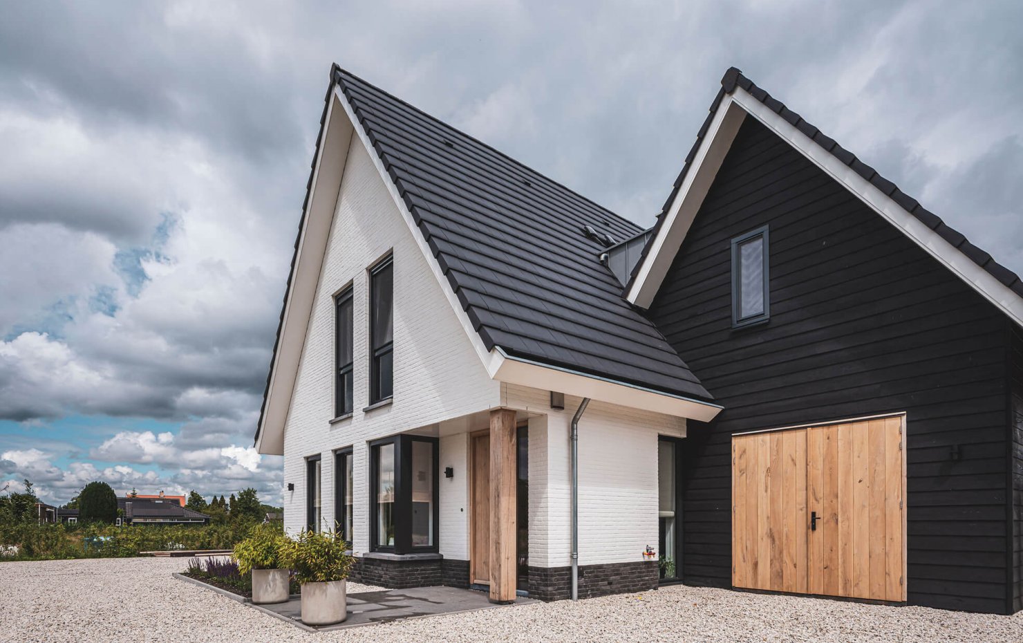 Witte gevelsteen naast zwarte gevelbetimmering met stoere houten deuren