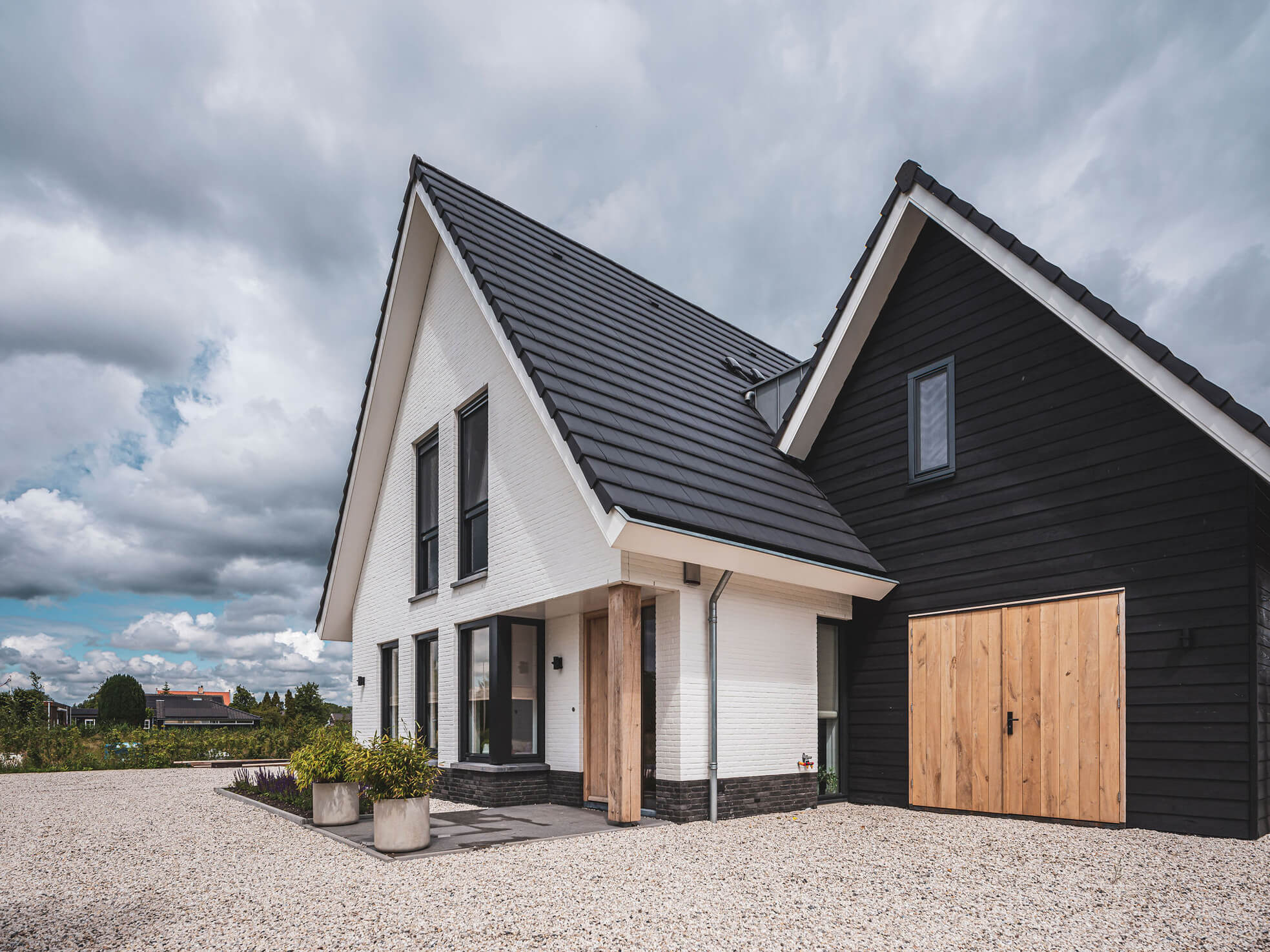 Witte gevelsteen naast zwarte gevelbetimmering met stoere houten deuren