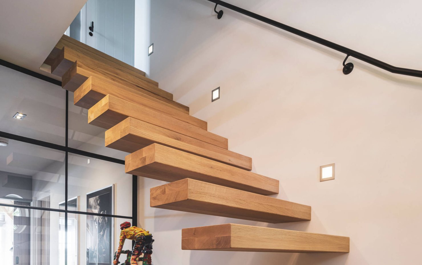 Zwevende trap van massief hout met spots in de wand