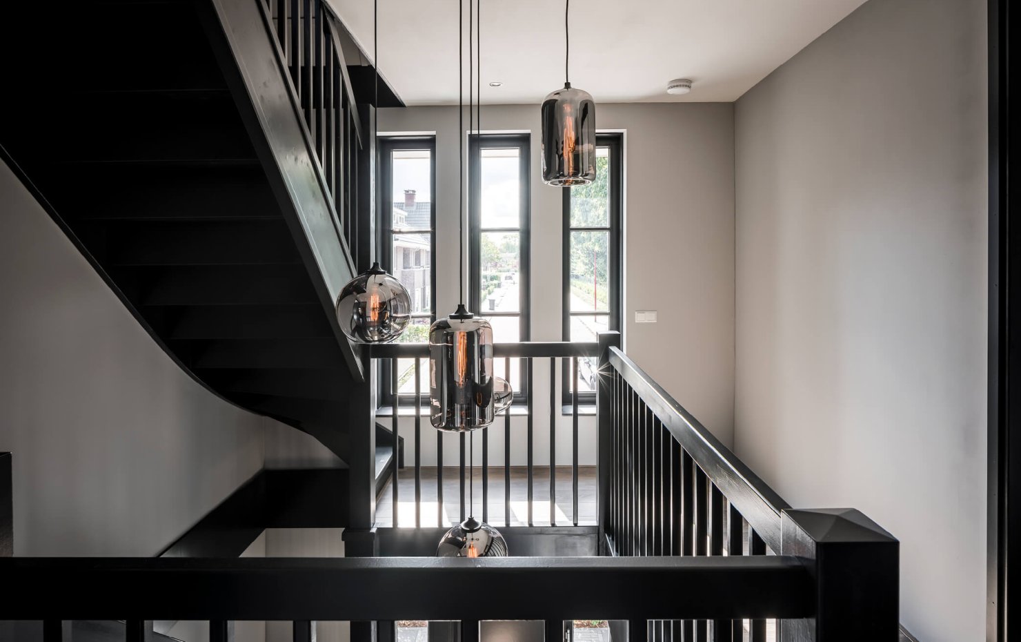 Overloop herenhuis met design lampen en stoere houten balustrade bij de trappen