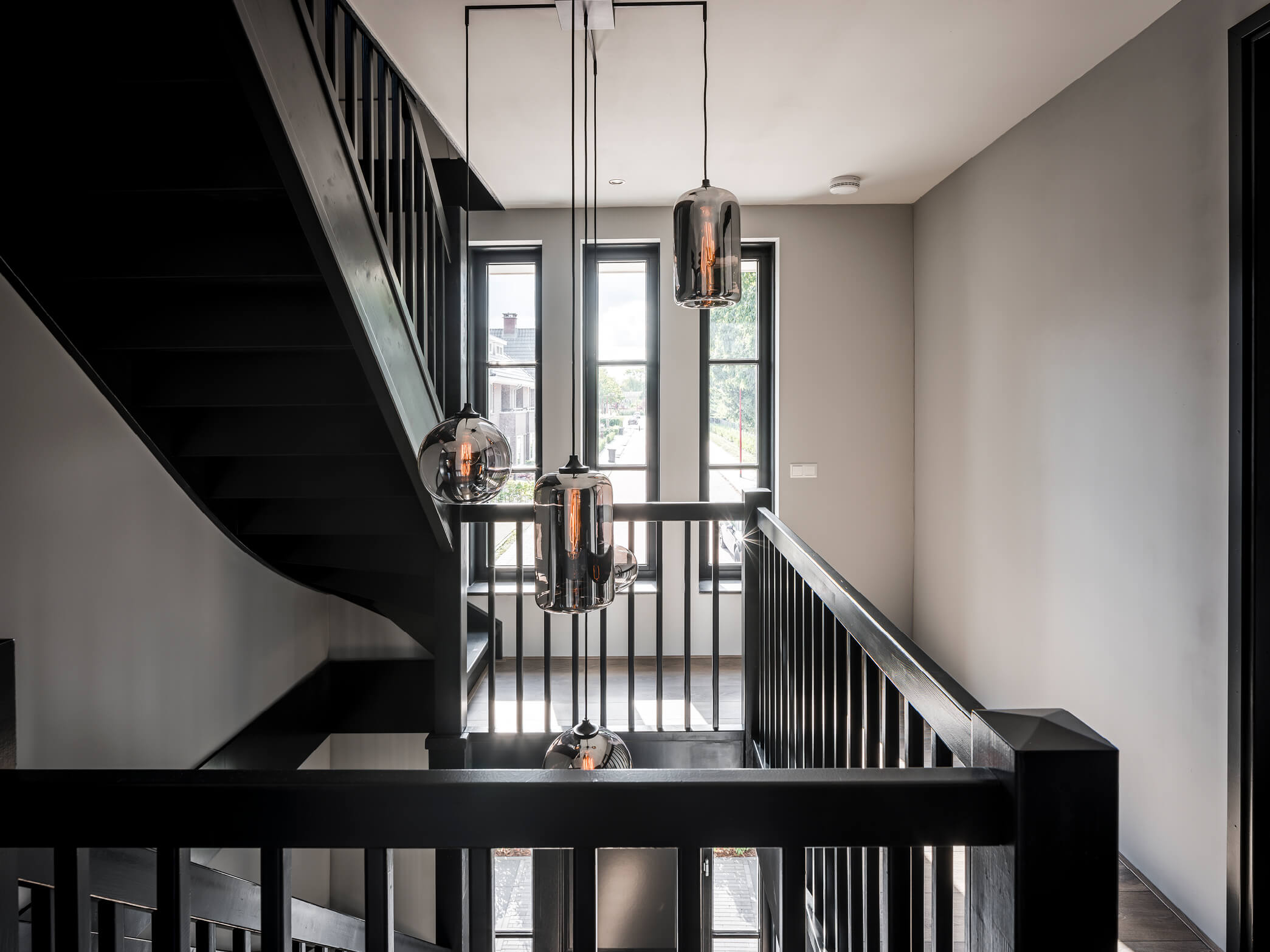 Overloop herenhuis met design lampen en stoere houten balustrade bij de trappen