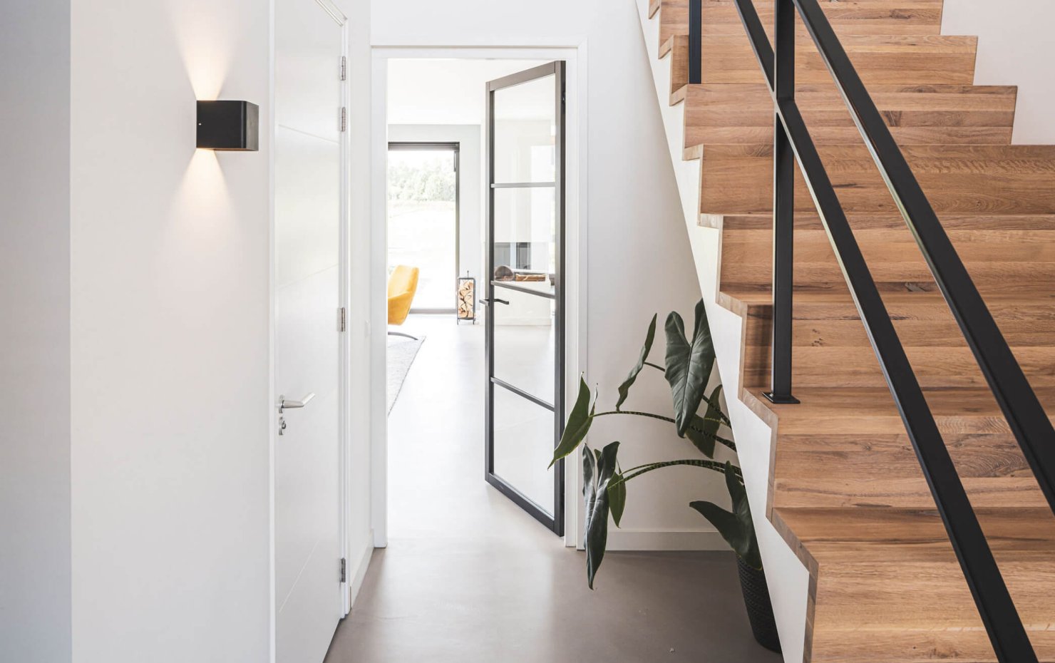 Lichte hal met stalen binnendeur naar de living en maatwerk houten trap