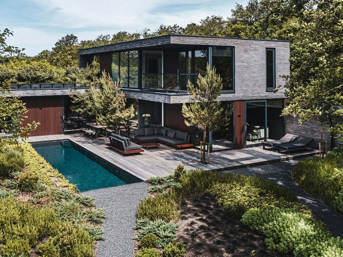 Bovenaanzicht moderne kubistische villa met houten gevel, zwembad, terras, en omringd door groen