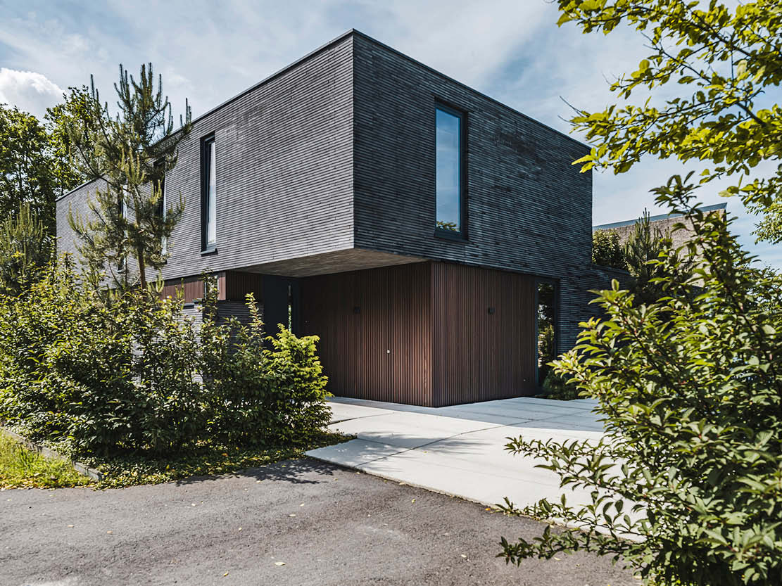 Moderne kubistische villa met donkere houten gevel en opvallende vorm.