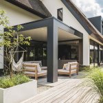 ThumbnailBuitenfoto van een rietgedekt huis met een modern terras, houten zitmeubels en schaduwrijke veranda.