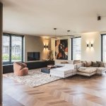 ThumbnailInterieurfoto van een moderne woonkamer met een opvallend kunstwerk aan de muur, een hoekbank, fauteuil en een houten parketvloer.