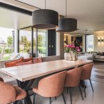ThumbnailInterieurfoto van een woonkamer met een houten eettafel met oranje stoelen, grijze hanglampen, bank met kussens en grote schuifdeuren.
