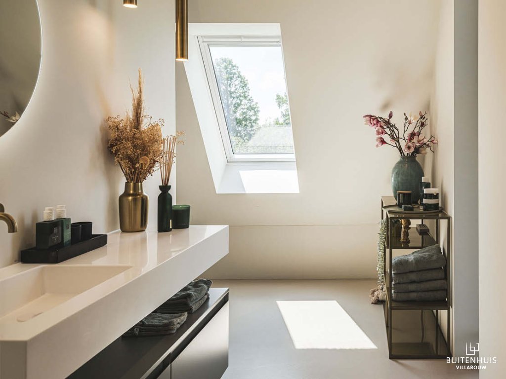ThumbnailInterieurfoto van een moderne badkamer met witte wastafel, gouden kraan, dakraam en decoratieve vazen.