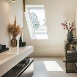 ThumbnailInterieurfoto van een moderne badkamer met witte wastafel, gouden kraan, dakraam en decoratieve vazen.