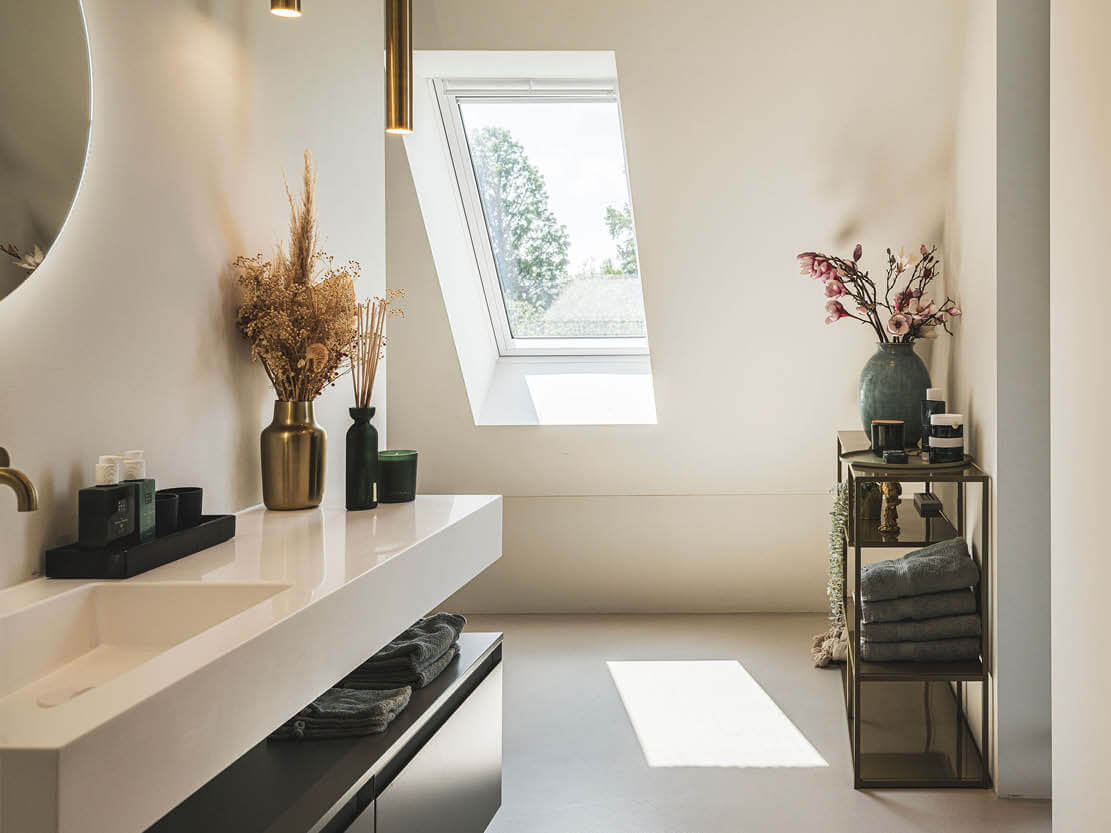 Interieurfoto van een moderne badkamer met witte wastafel, gouden kraan, dakraam en decoratieve vazen.